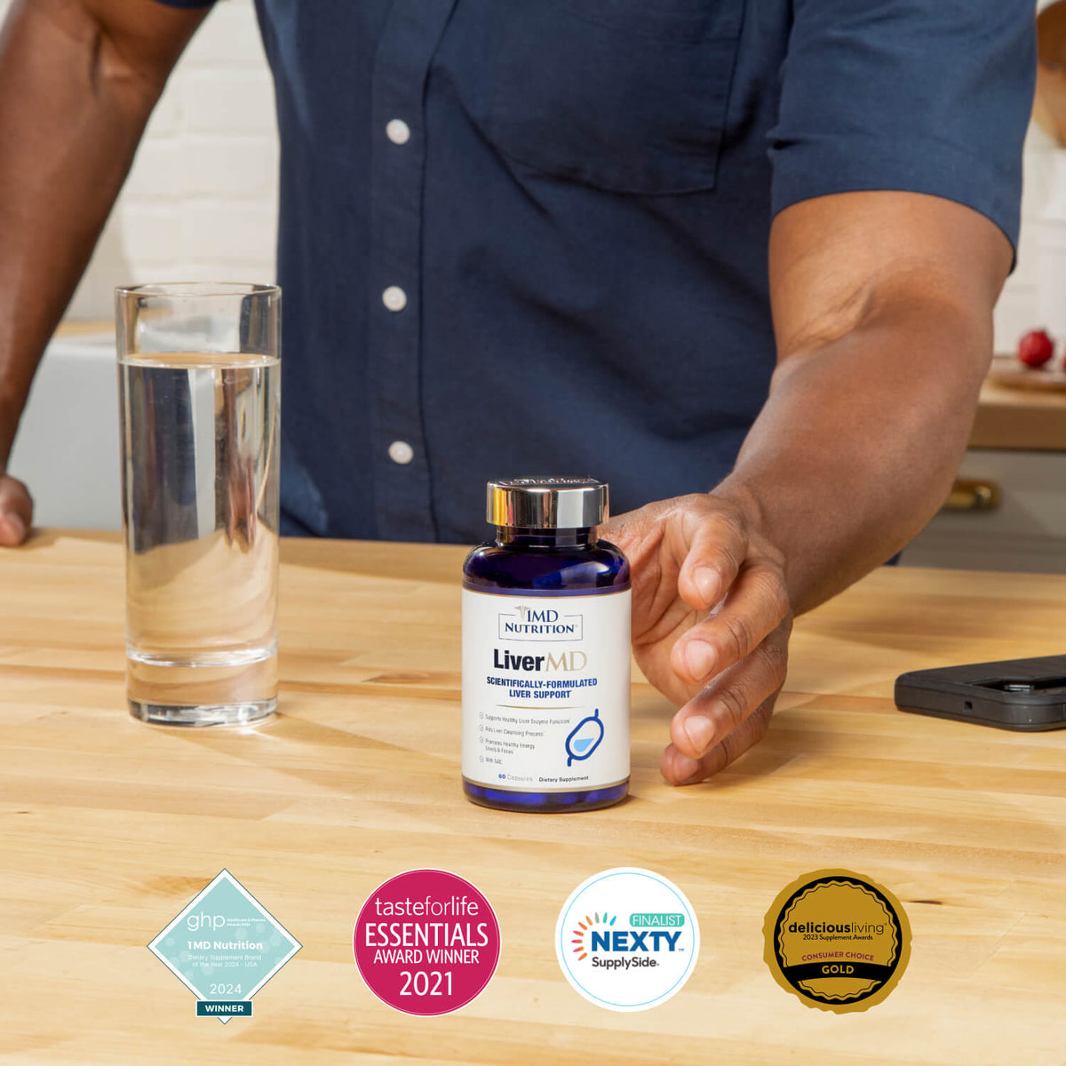 Man reaching for a bottle of LiverMD liver support capsules on a kitchen counter beside a glass of water